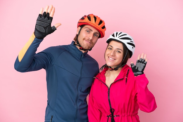 Junge kaukasische radfahrer, die auf rosa hintergrund isoliert sind und mit der hand mit glücklichem ausdruck salutieren