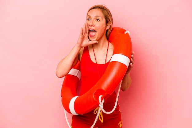Junge kaukasische Rettungsschwimmerin isoliert auf rosa Hintergrund schreit und hält Handfläche in der Nähe des geöffneten Mundes