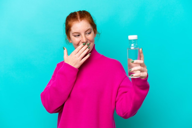 Junge kaukasische rötliche Frau mit einer Flasche Wasser isoliert auf blauem Hintergrund mit Überraschung und schockiertem Gesichtsausdruck