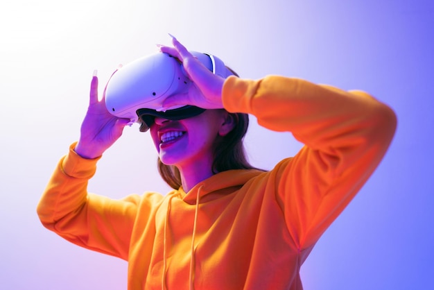 Junge kaukasische schöne Frau mit gelbem Hoodie und VR-Headset, die virtuelle Realität mit einem roten und blauen Neonlicht im Hintergrund erlebt futuristische Technologie und tragbares Gerätekonzept