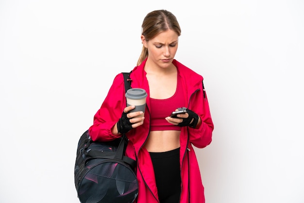 Junge kaukasische Sportlerin isoliert auf weißem Hintergrund mit Kaffee zum Mitnehmen und einem Handy