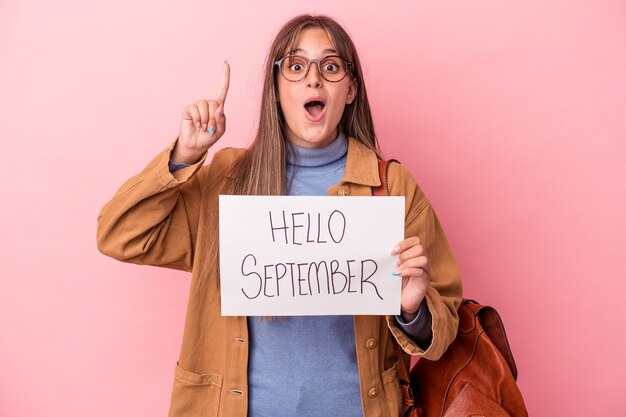 Junge kaukasische Studentenfrau, die hallo September-Plakat einzeln auf rosa Hintergrund hält und eine Idee, Inspirationskonzept hat.