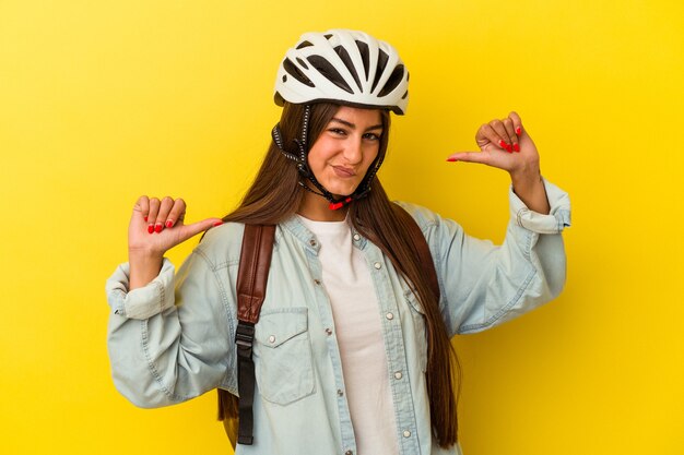 Foto junge kaukasische studentin, die einen fahrradhelm einzeln auf gelbem hintergrund trägt, fühlt sich stolz und selbstbewusst, beispiel zu folgen.