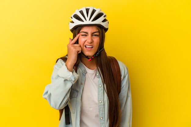 Junge kaukasische Studentin, die einen Fahrradhelm trägt, der auf gelbem Hintergrund isoliert ist und eine Enttäuschungsgeste mit dem Zeigefinger zeigt.