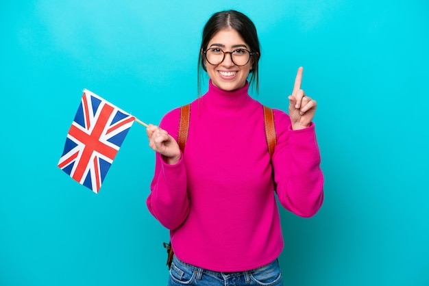 Junge kaukasische Studentin mit englischer Flagge isoliert auf blauem Hintergrund, die auf eine großartige Idee zeigt