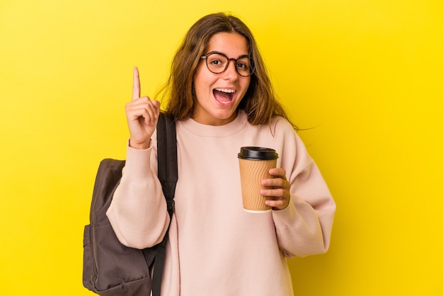 Junge kaukasische Studentin mit Kaffee isoliert auf gelbem Hintergrund mit einer Idee, Inspirationskonzept.