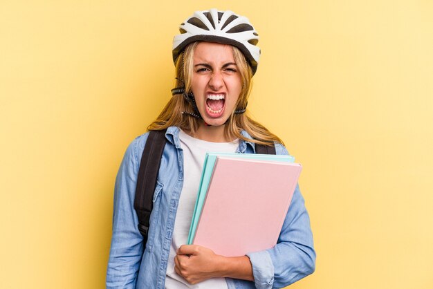 Junge kaukasische Studentin trägt einen Fahrradhelm einzeln auf gelbem Hintergrund und schreit sehr wütend und aggressiv.