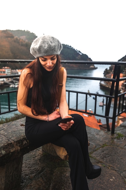 Junge kaukasische Touristenfrau mit dem Smartphone saß auf einer Bank neben dem Meer.