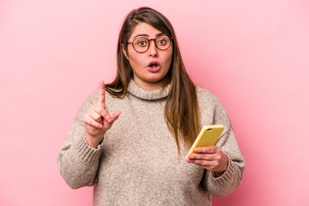 Junge kaukasische übergewichtige Frau mit einem Handy isoliert auf rosa Hintergrund mit einer großartigen Idee, Konzept der Kreativität.