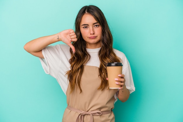 Junge kaukasische Verkäuferin, die einen Kaffee zum Mitnehmen hält, isoliert auf blauem Hintergrund, der eine Abneigungsgeste zeigt, Daumen nach unten. Meinungsverschiedenheit Konzept.