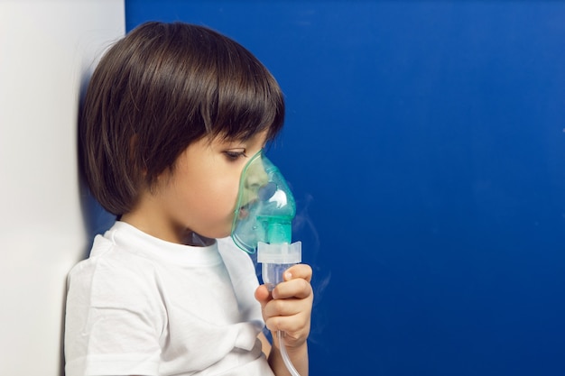 Junge kind unterzieht sich behandlung atmet inhalation grüne maske an der wand einer blauen wand in einer kinderklinik