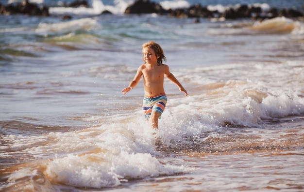 Junge Kinder, die in Meereswellen springen, springen durch Wassermeerspritzer Sommerkinderferien