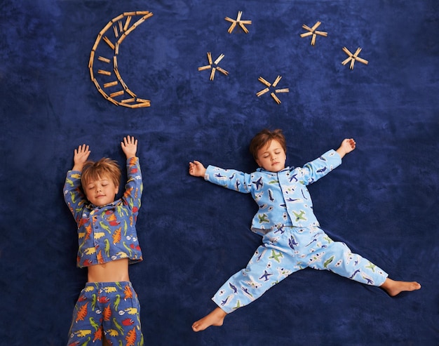 Foto junge kinder im schlafanzug schlafen auf einem teppich mit mond- und sternendesign von oben und kleine kinder träumen. frieden, ruhe und müde brüder oder freunde schlafen auf galaxienkunst auf einer matte im zuhause der familie