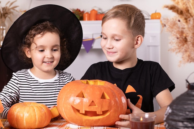 Junge Kinder, Mädchen und Jungen, die traditionelle Halloween-Jackolanterns mit gruseligem Gesicht für die Party zu Hause schnitzen