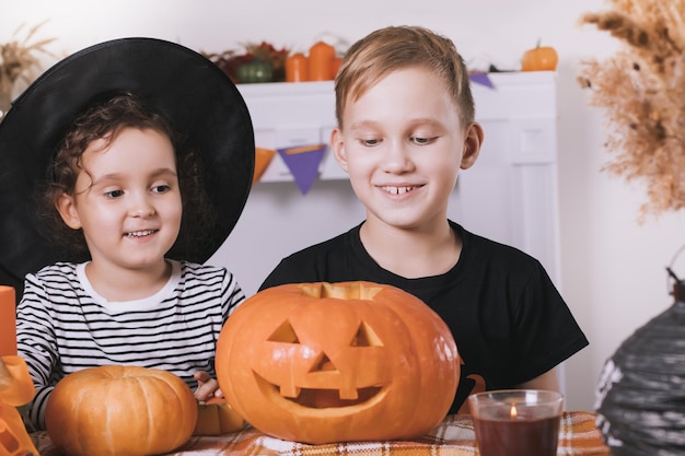 Junge Kinder, Mädchen und Jungen, die traditionelle Halloween-Kürbislaternen mit gruseligem Gesicht für die Party zu Hause schnitzen.