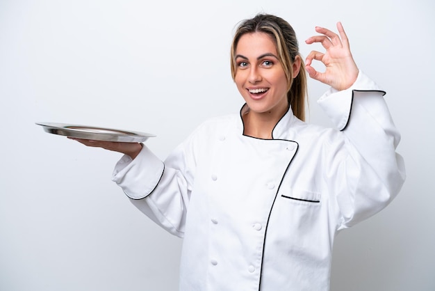 Junge Köchin mit Tablett isoliert auf weißem Hintergrund mit OK-Zeichen mit den Fingern