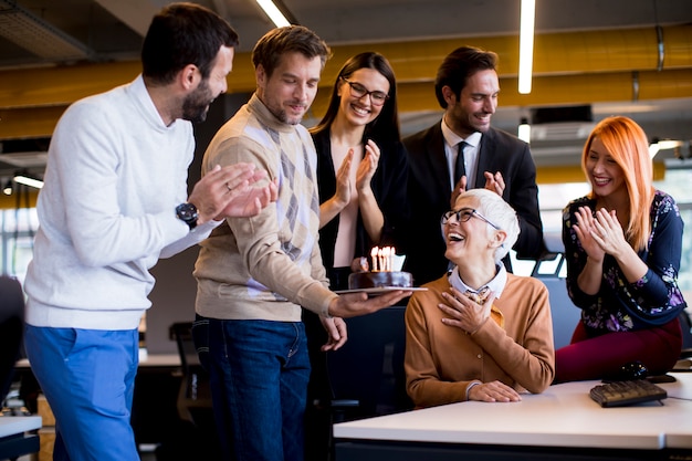 Junge Kollegen feiern im Büro den Geburtstag eines älteren Kollegen und bringen einen Kuchen mit