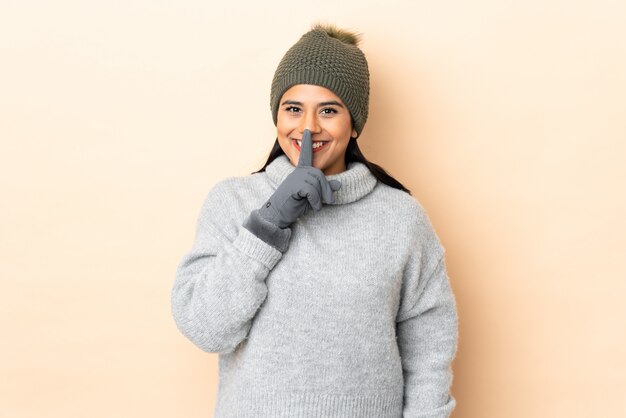 Foto junge kolumbianische frau mit wintermütze lokalisiert auf beige wand, die schweigegeste tut