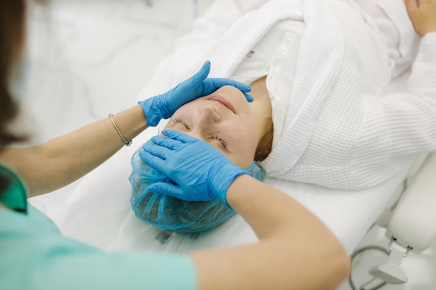 Junge Kosmetikerin in Maske trägt Kontaktgel auf das Bein einer Frau zur Laser-Haarentfernung auf