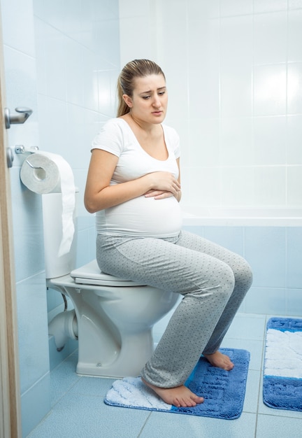 Junge kranke schwangere Frau, die auf der Toilette witzelt