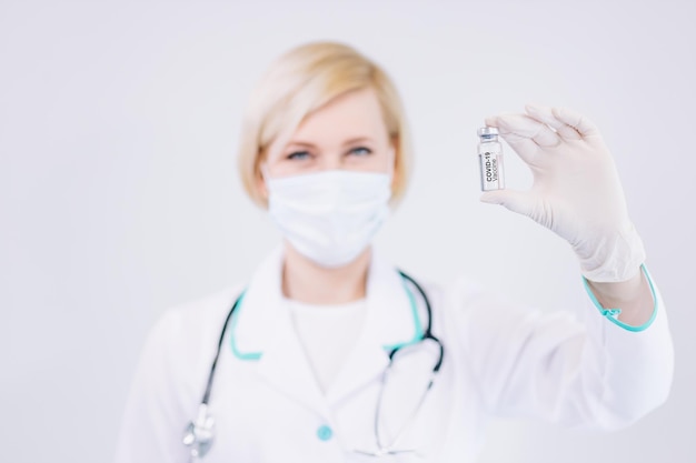 Junge Krankenschwester Ärztin, die einen klaren flüssigen Impfstoff in der Hand hält, um sich vor Covid19 zu schützen