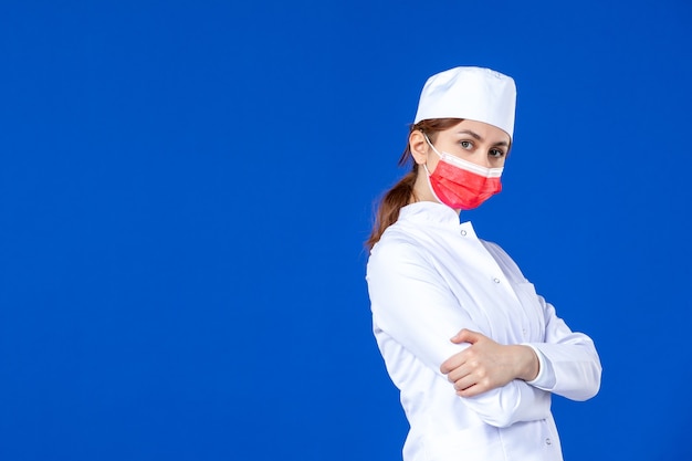 Junge Krankenschwester der Vorderansicht im medizinischen Anzug mit roter Maske auf blauer Wand