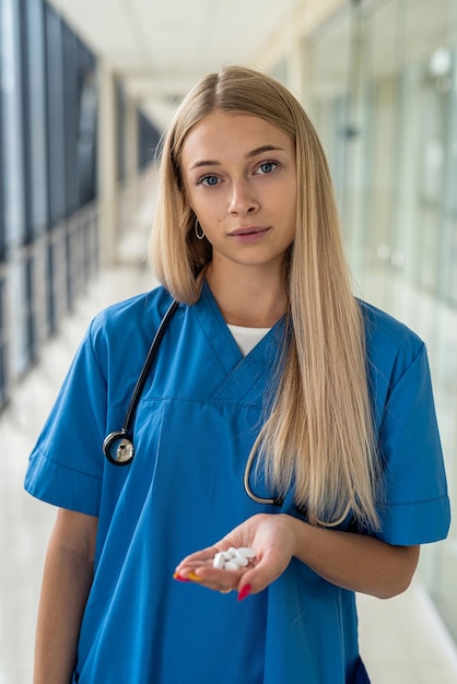 Junge Krankenschwester, die im Flur eine weiße Pille in der Hand hält