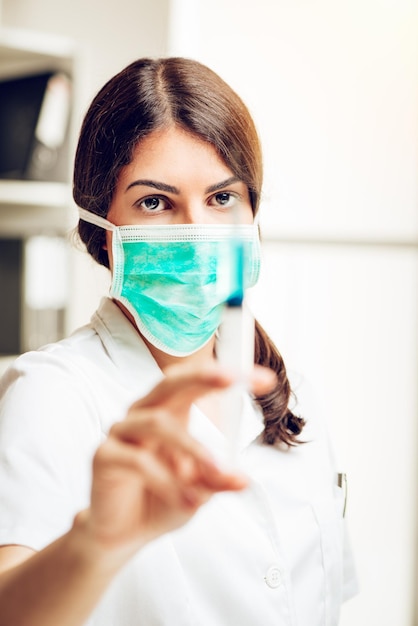 Junge Krankenschwester, die in ihrem Sprechzimmer steht und eine Anästhesie-Injektion vorbereitet. Selektiver Fokus. Konzentrieren Sie sich auf den Hintergrund, auf die Krankenschwester.