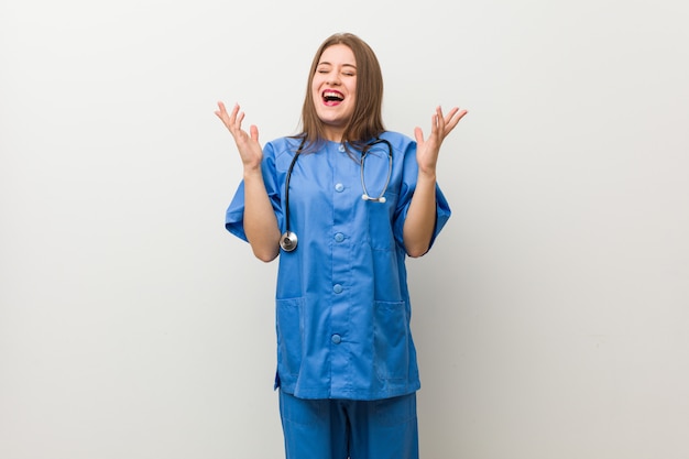 Junge Krankenschwester Frau gegen eine weiße Wand freudig viel lachen. Glückskonzept.