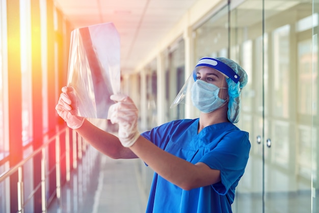 Junge Krankenschwester in blauer einheitlicher Schutzmaske und Gesichtsschutz betrachtet das Ergebnis der Lungenfluorographie