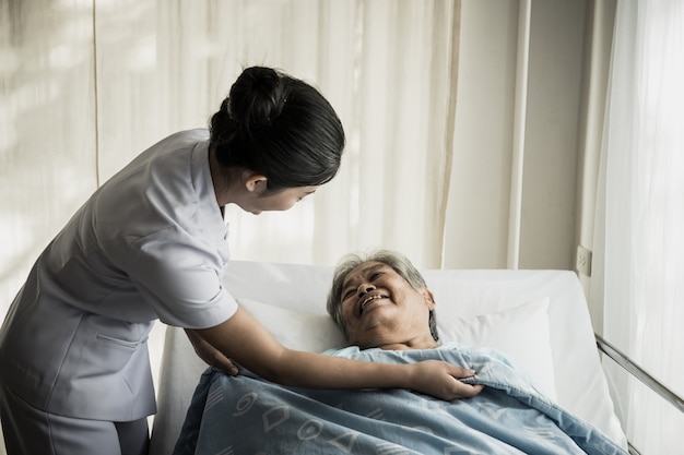 Junge Krankenschwester kümmern sich um älteren Patienten im Krankenhauszimmer