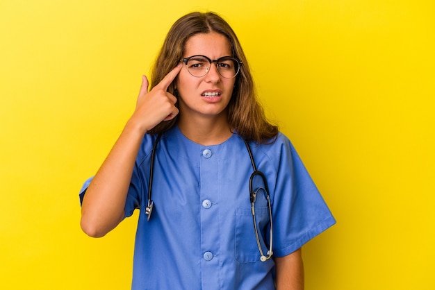 Junge Krankenschwesterfrau lokalisiert auf gelbem Hintergrund, der eine Enttäuschungsgeste mit dem Zeigefinger zeigt.