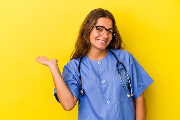 Junge Krankenschwesterfrau lokalisiert auf gelbem Hintergrund, der einen Kopienraum auf einer Palme zeigt und eine andere Hand auf Taille hält.