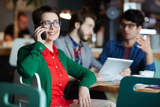 Junge kreative Geschäftsfrau, die durch Smartphone spricht