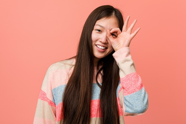 Junge kühle chinesische Frau aufgeregt, okaygeste auf Auge halten.