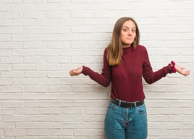 Junge kühle Frau über einer Backsteinmauer, die Schultern zweifelt und zuckt