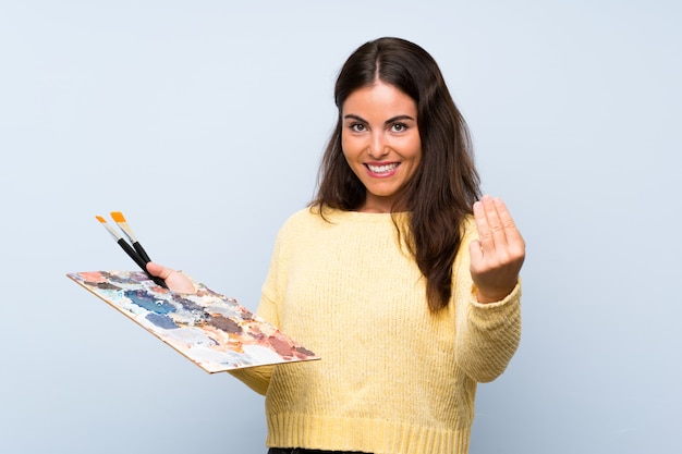 Junge Künstlerfrau über der lokalisierten blauen Wand, die einlädt, mit der Hand zu kommen, glücklich, dass Sie kamen