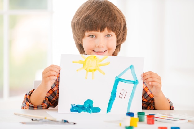 Junge Künstlerin. Fröhlicher kleiner Junge, der sich beim Malen mit Aquarellen am Tisch entspannt