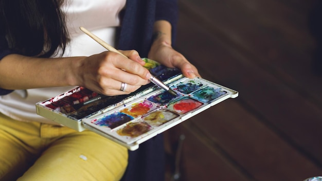 Junge Künstlerin zeichnet Bilder mit Aquarellfarben und Pinsel, die Farben in Nahaufnahme mischen