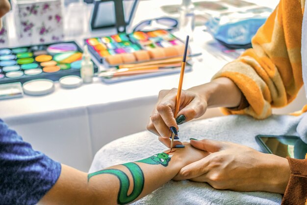 Junge Künstlerin zeichnet einen Drachen auf die Hand des Kindes und malt die Haut mit Farben