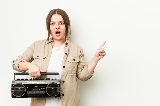 Junge kurvige Frau, die ein Retro-Radio hält, das zur Seite zeigt