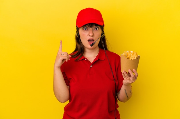 Junge kurvige kaukasische Frau Fast-Food-Restaurant-Arbeiter mit Pommes auf blauem Hintergrund isoliert mit einer Idee, Inspirationskonzept.