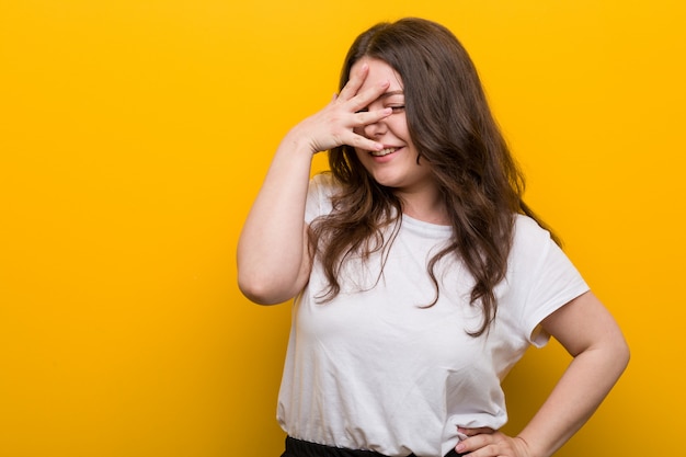 Junge kurvige Plusgrößenfrau blinzeln in die Kamera durch die Finger, verlegenes Bedeckungsgesicht.