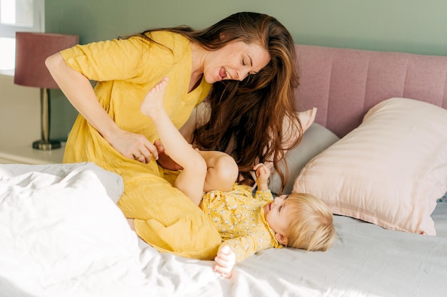 Junge lachende Mutter kitzelt ihre spielende Tochter im Bett