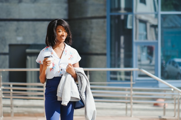 junge lächelnde afroamerikanische Geschäftsfrau mit Kaffeetasse in der Stadt