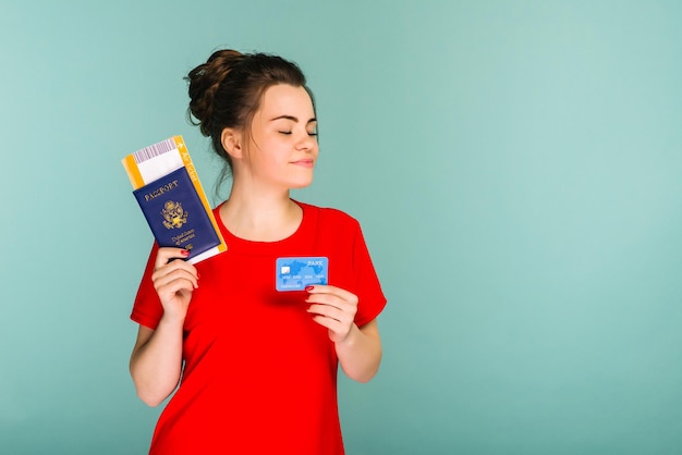Junge, lächelnde, aufgeregte Frau, Studentin mit Reisepass, Bordkarte, Ticket und Kreditkarte, isoliert auf blauem Hintergrund, Flugzeug.
