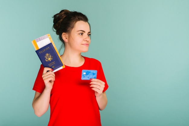 Junge lächelnde aufgeregte Studentin, die Pass-Bordkarte und Kreditkarte hält
