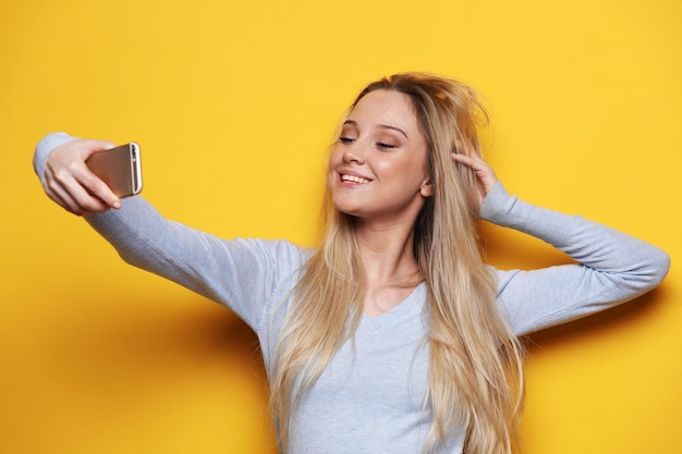 Junge lächelnde blonde Frau macht Selfie auf gelbem Hintergrund