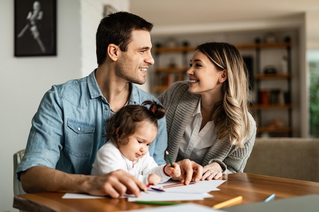 Junge lächelnde Eltern kommunizieren beim Malen auf dem Papier mit ihrer Tochter zu Hause