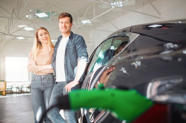 Junge lächelnde Familie, die erstes Elektroauto im Ausstellungsraum kauft